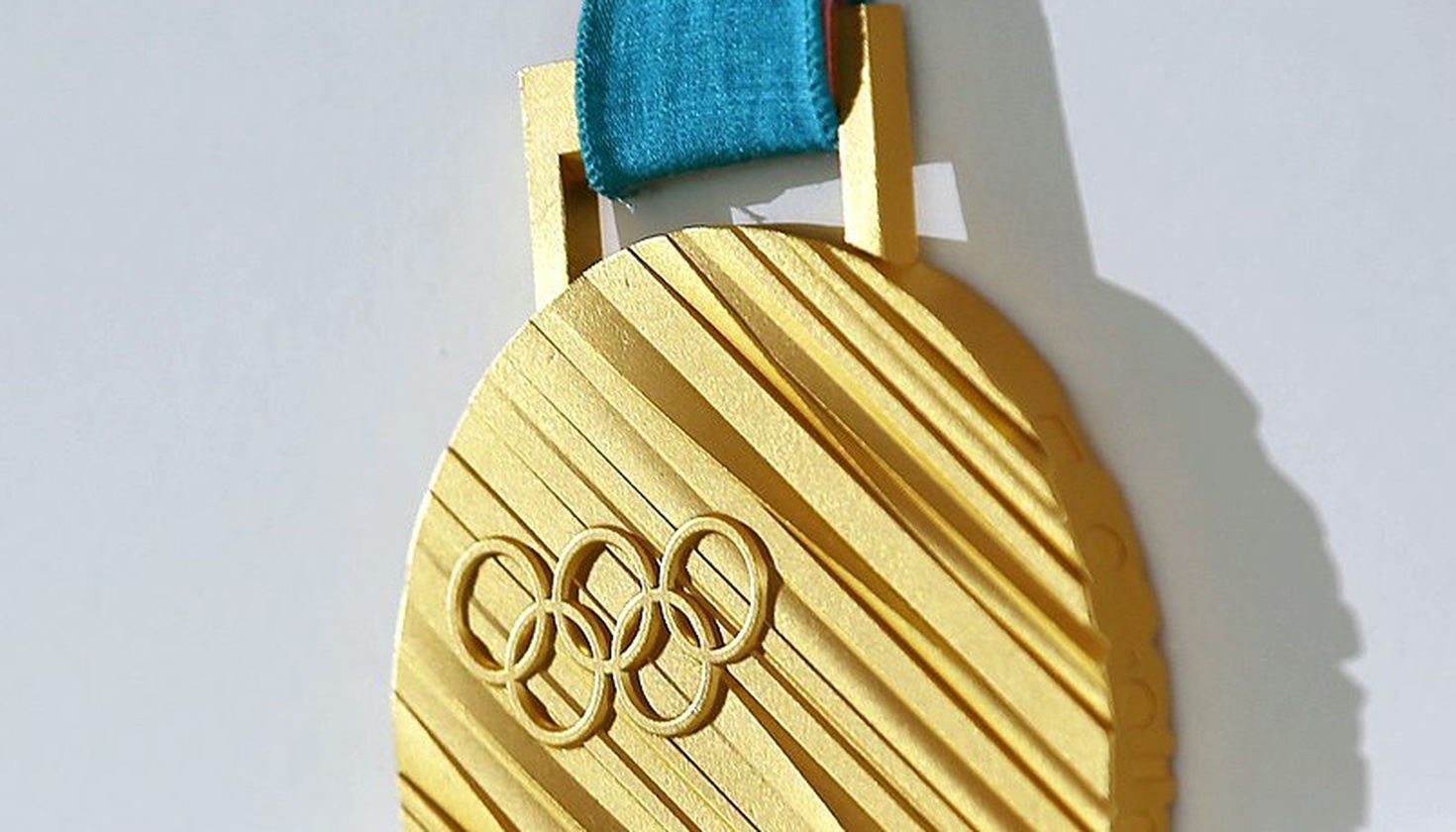 Close-up of a gold medal from the 2018 PyeongChang Olympics, showing a ridge-textured golden surface upon which the Olympic rings are set.